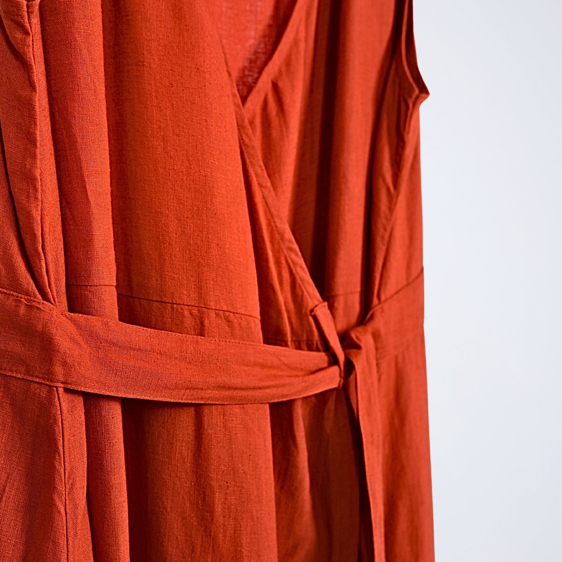 Sleeveless linen dress with pleated wrap fall. Breathable, relaxed, and fluid for moving forward with ease