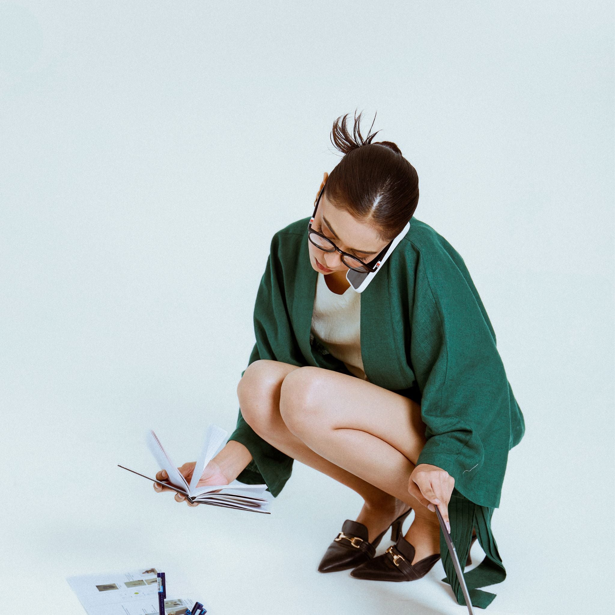 Woman in green coat reading a book on a light blue background