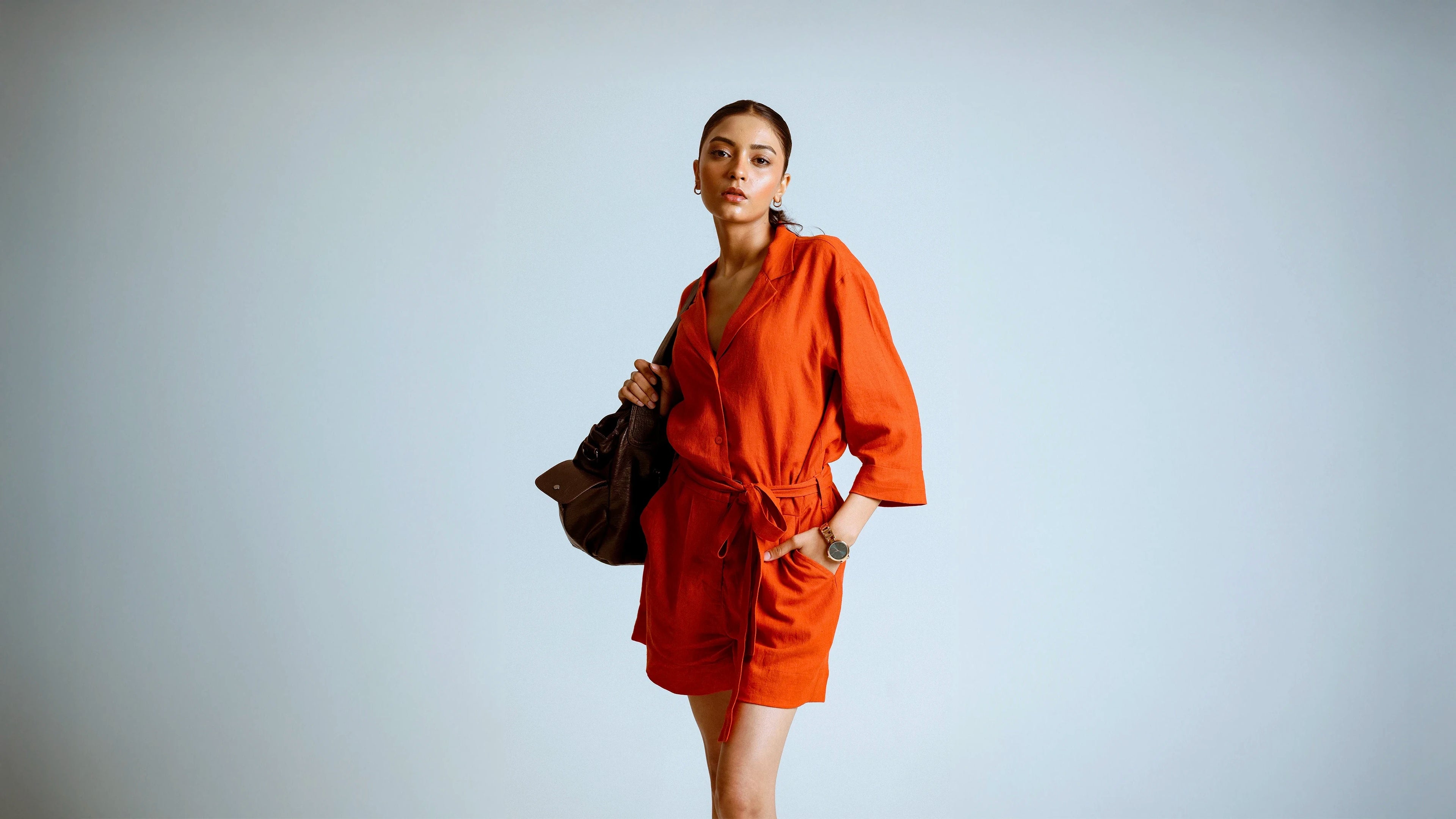 Person wearing an orange jumpsuit holding a black bag against a plain background
